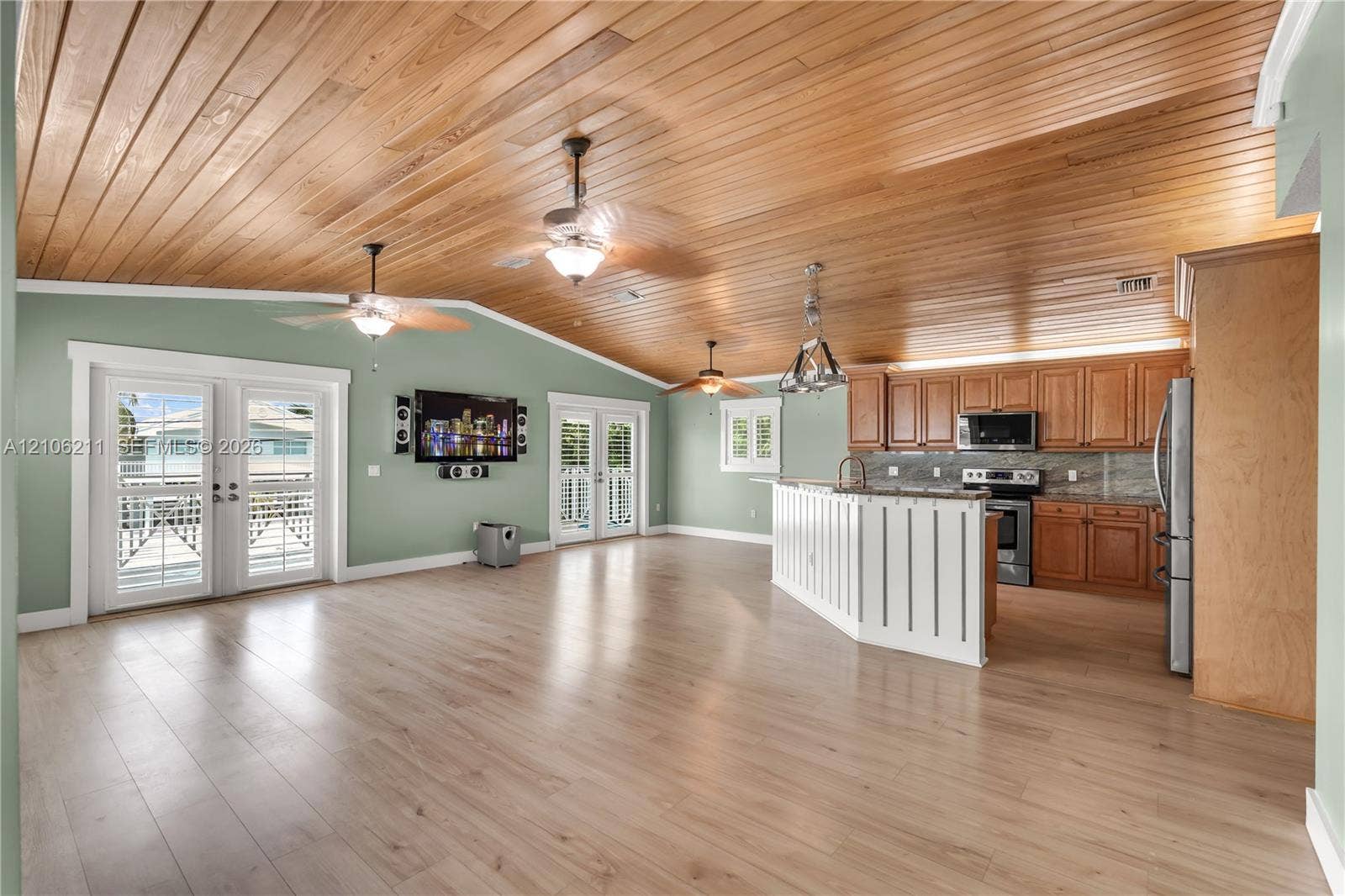Vaulted wood-plank ceiling, wood-finish flooring, kitchen featuring a white paneled peninsula with stone countertops, and double glass-paned doors with shutters