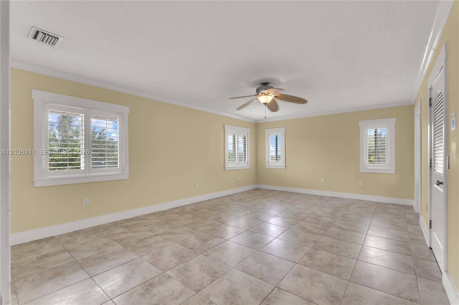 Neutral-toned interior room featuring large-format ceramic tile flooring, plantation shutters, and a ceiling fan with integrated lighting
