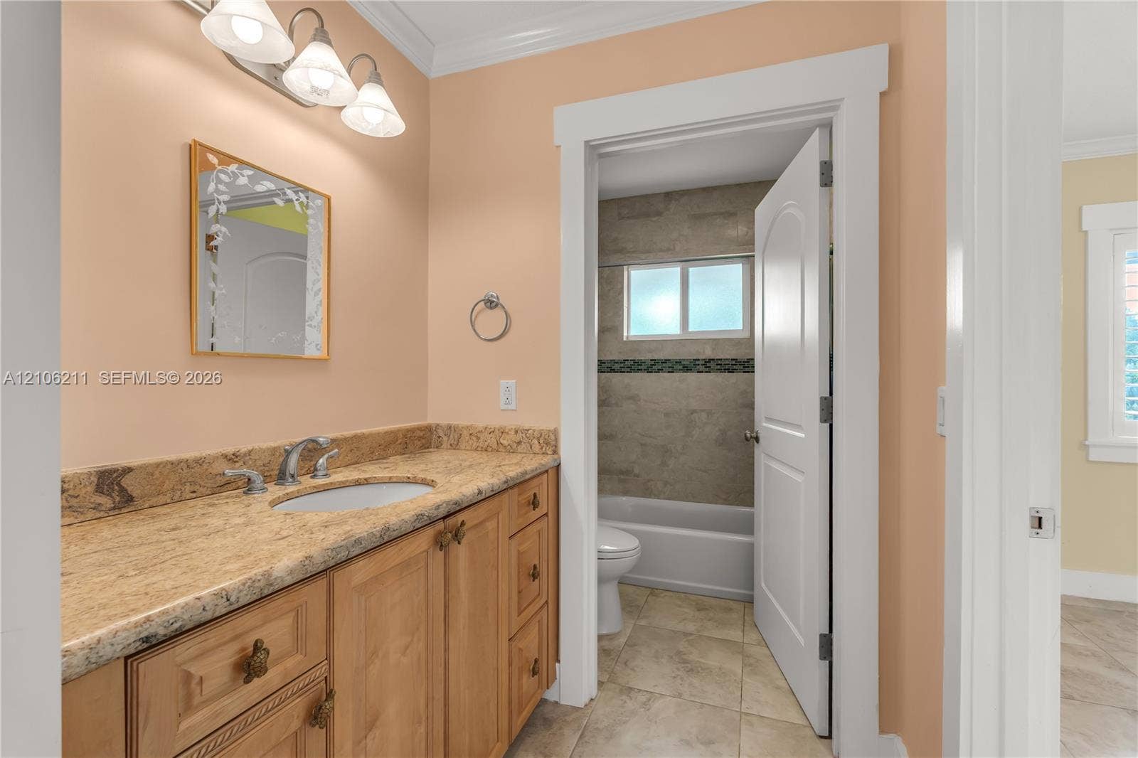 Vanity featuring stone-finish countertop, undermount sink, and wood cabinetry, complemented by a three-light fixture and tile flooring