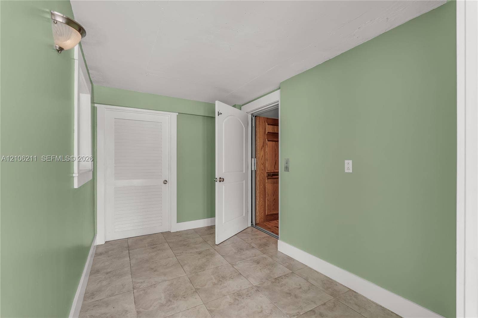 Interior space featuring tile flooring, louvered closet door, arched panel door, and integrated home elevator