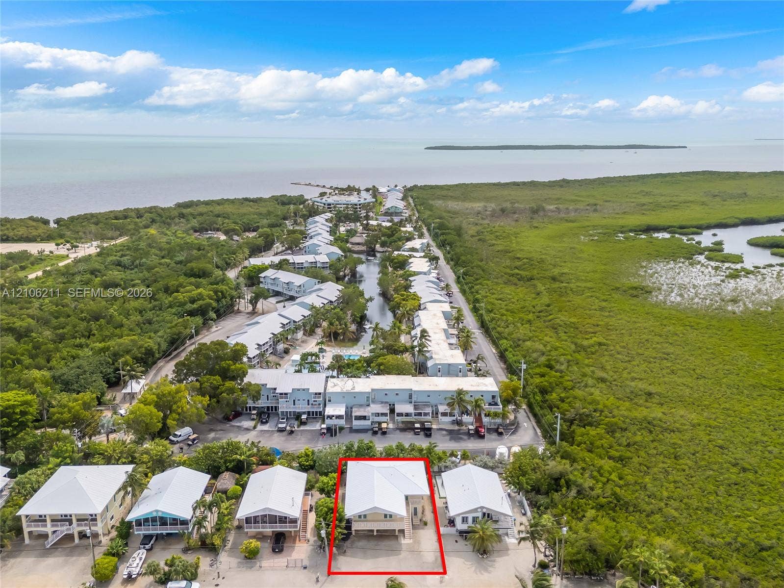 Aerial perspective of coastal residential property featuring a metal roof, elevated foundation, covered ground-level parking, and native landscaping