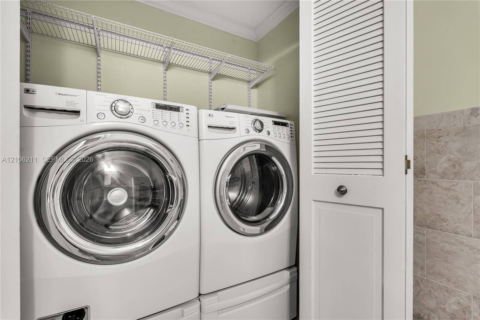 Laundry area featuring wall-mounted wire shelving, louvered closet doors, and tile wall surfacing