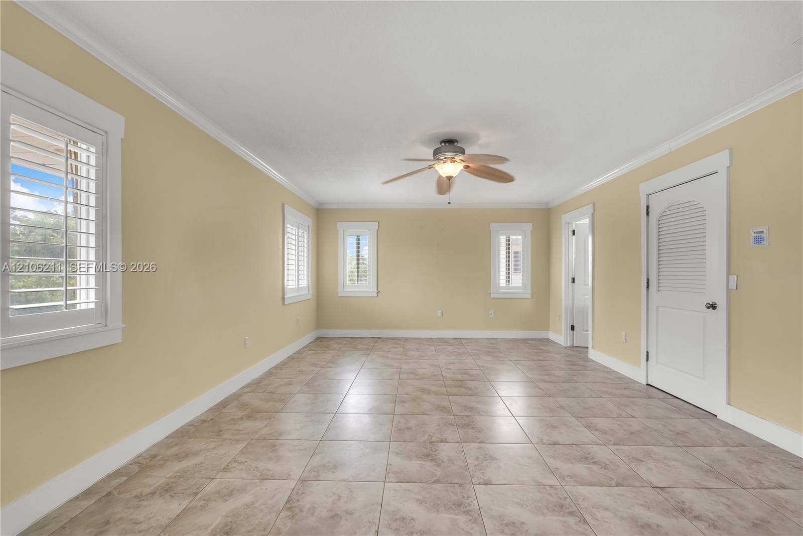 Spacious interior featuring neutral wall tones, ceramic tile flooring, plantation shutters, crown molding, and a central ceiling fan with an integrated light fixture