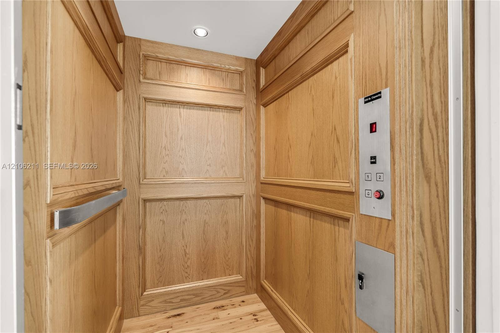 Private elevator featuring wood-paneled walls with decorative molding, brushed metal control panel, and a stainless steel grab bar