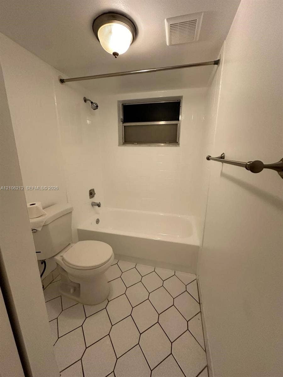 Bathroom featuring a white porcelain tub with integrated shower surround, hexagonal floor tile, chrome-finished hardware, and a semi-flush mount ceiling fixture