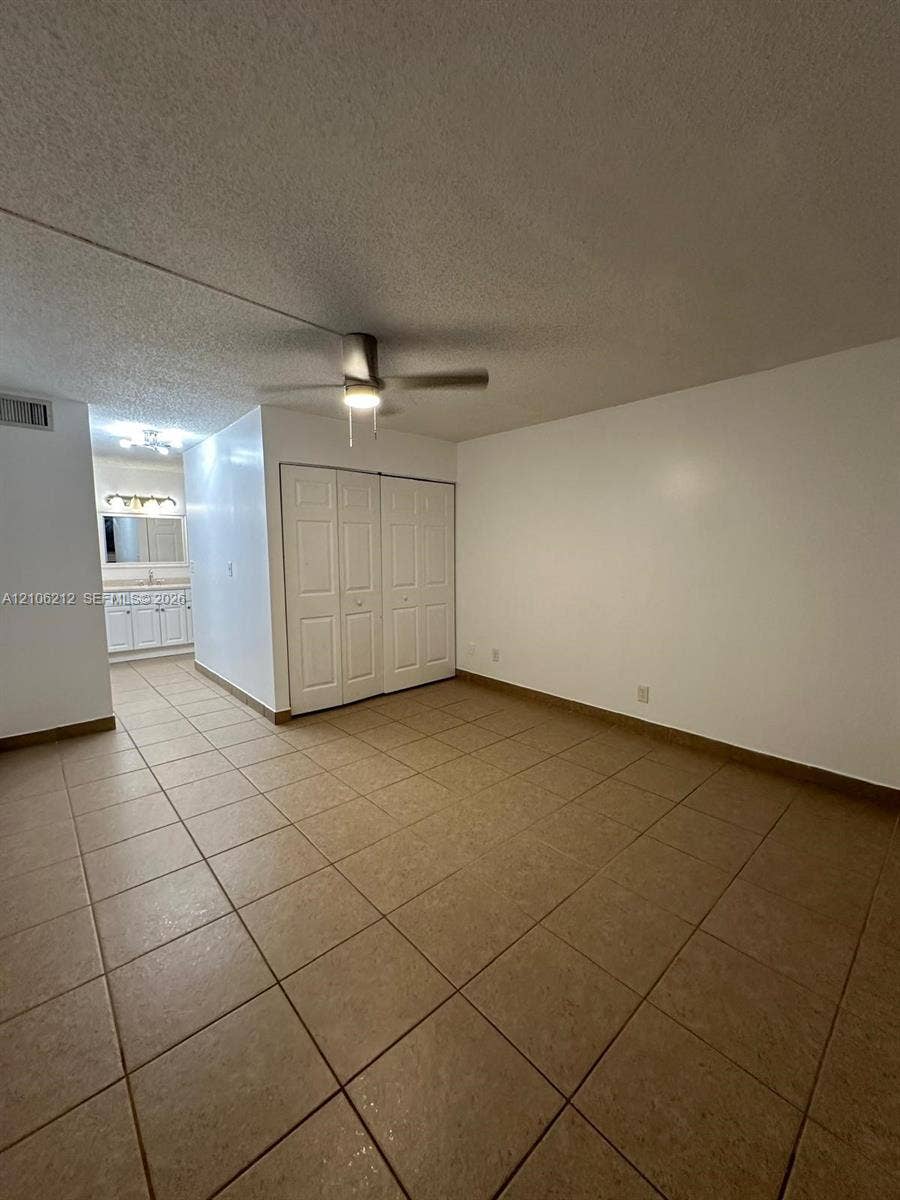 Neutral-toned ceramic tile flooring, ceiling fan with integrated lighting, dual-panel closet doors, and multi-light vanity fixture