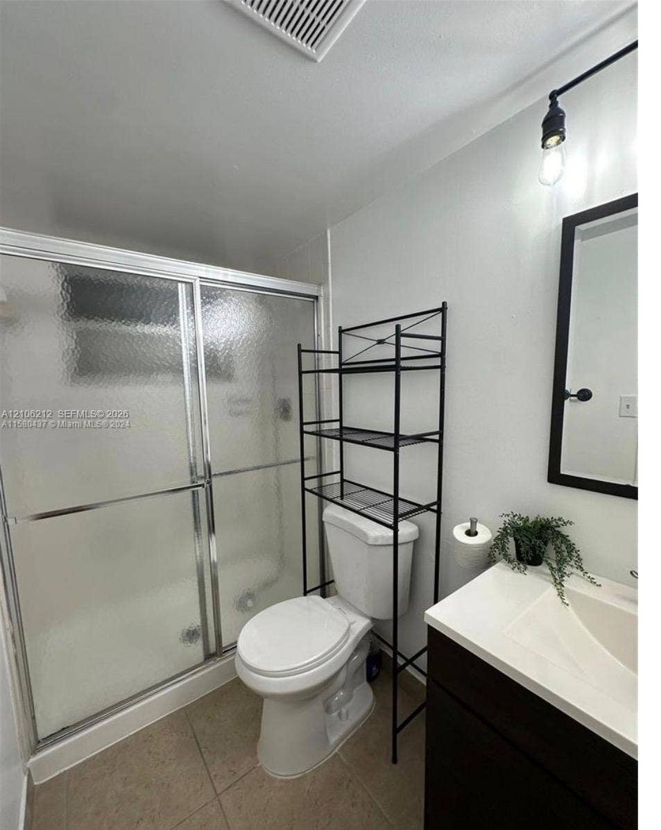 Shower enclosure with textured glass sliding doors, vanity featuring a white countertop with integrated sink, rectangular framed mirror, and matte black industrial-style wall-mounted lighting