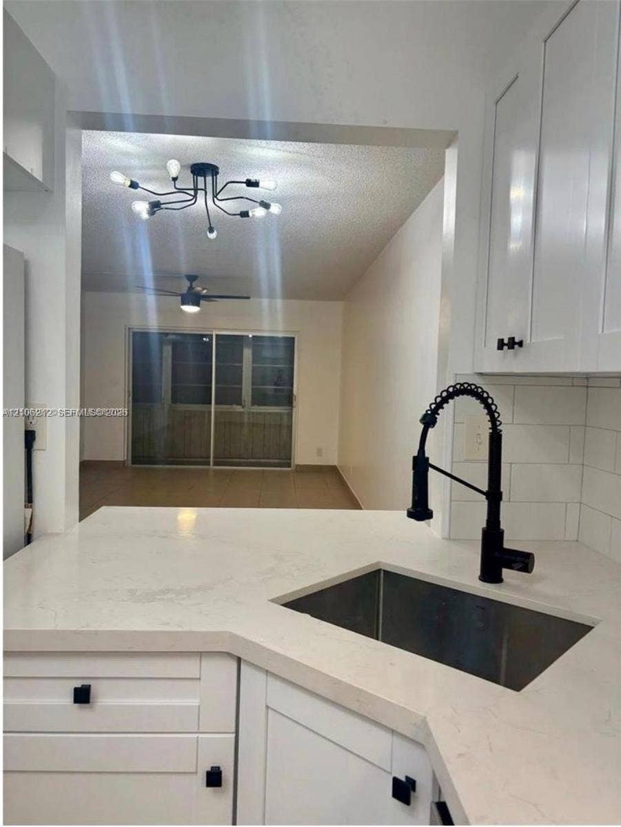 Kitchen featuring white shaker-style cabinetry, solid-surface countertops, a stainless steel undermount sink with a matte black pull-down faucet, and a white subway tile backsplash