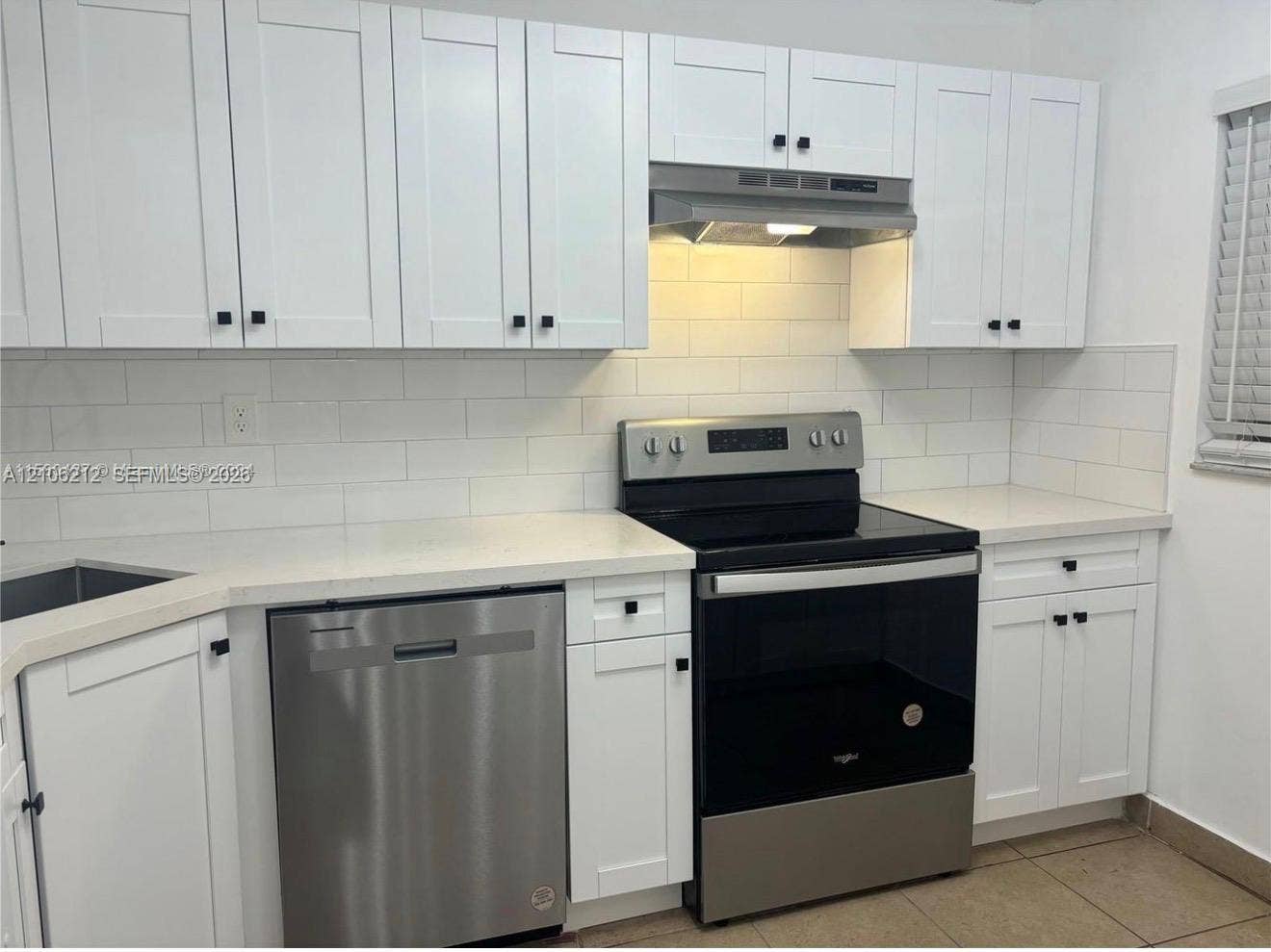 White shaker-style cabinetry, subway tile backsplash, solid-surface countertops, and stainless steel appliances