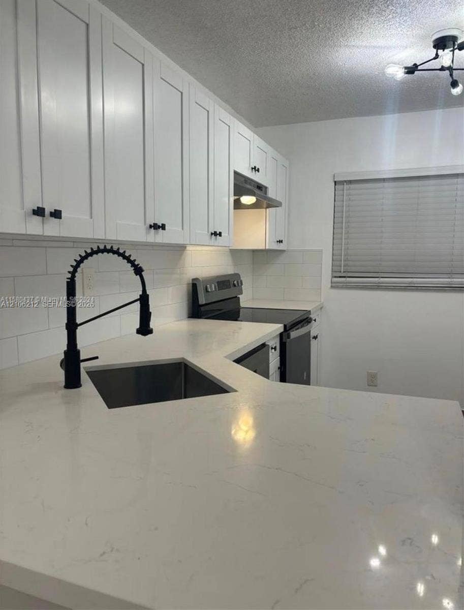 Kitchen featuring white shaker-style cabinetry, white countertops, a subway tile backsplash, a matte black gooseneck faucet, and a multi-bulb light fixture