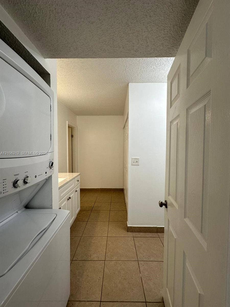 Laundry area featuring a stacked washer and dryer unit, neutral tile flooring, white cabinetry with a light-toned countertop, and a six-panel door