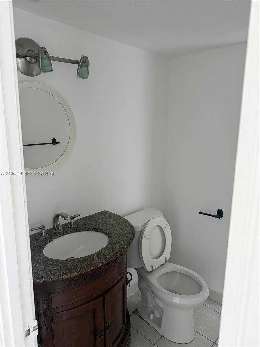 2841 NE 163rd Street, #305, North Miami Beach, North Miami Beach, FL 33160 Dark wood vanity with a stone countertop, oval undermount sink, circular wall mirror, two-light fixture, and ceramic tile flooring