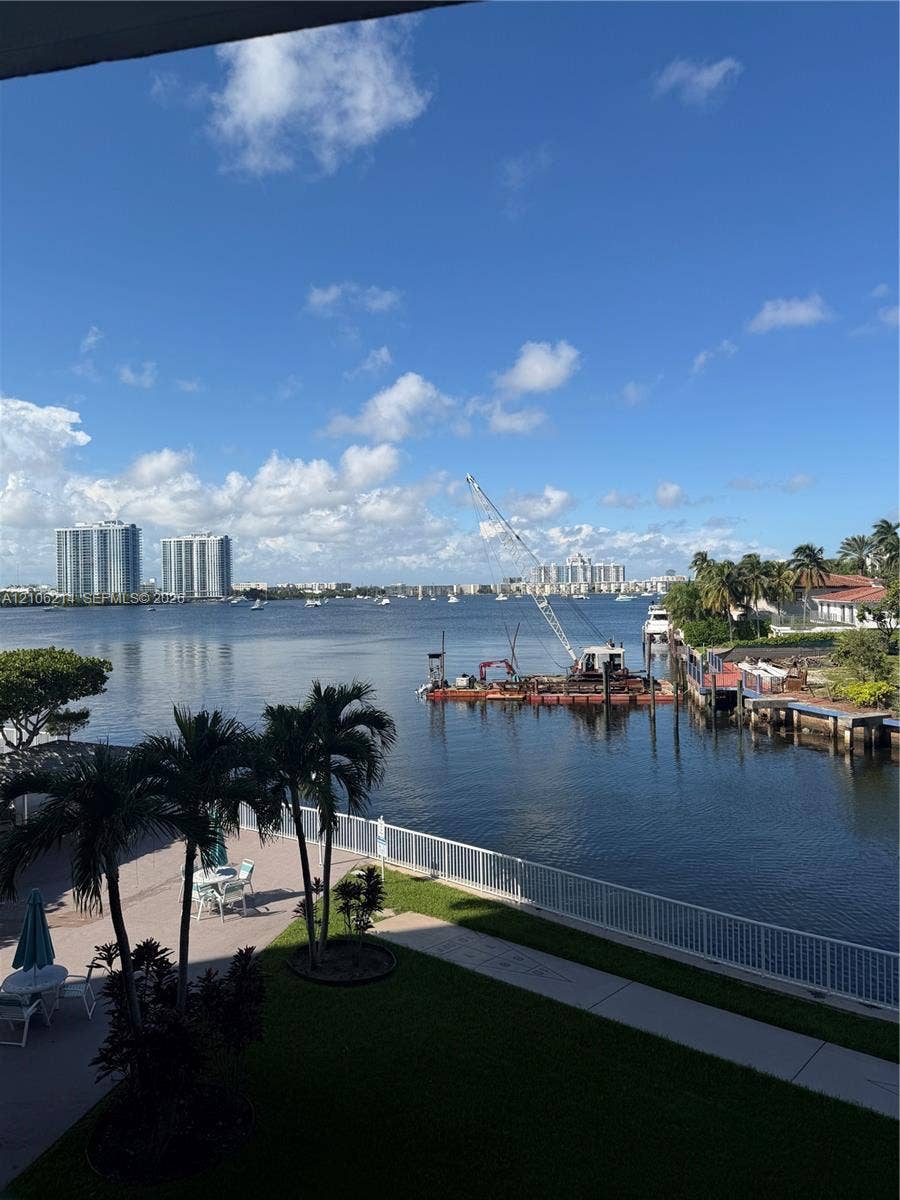 2841 NE 163rd Street, #305, North Miami Beach, North Miami Beach, FL 33160 Waterfront property featuring a paved patio, perimeter fencing, and mature palm trees