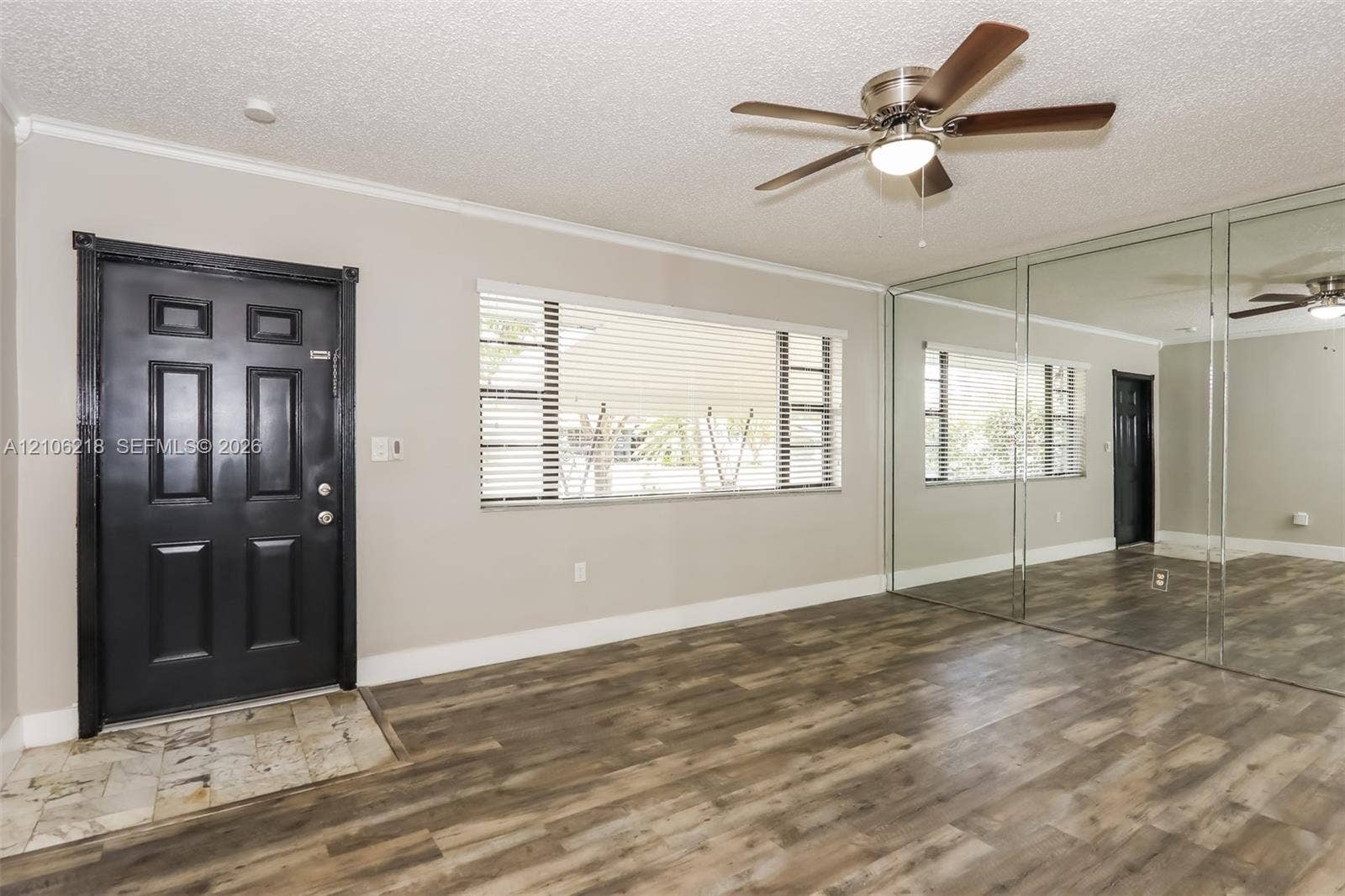 Wood-finish flooring, full-wall mirrored closet doors, ceiling fan with integrated lighting, and high-contrast entry door