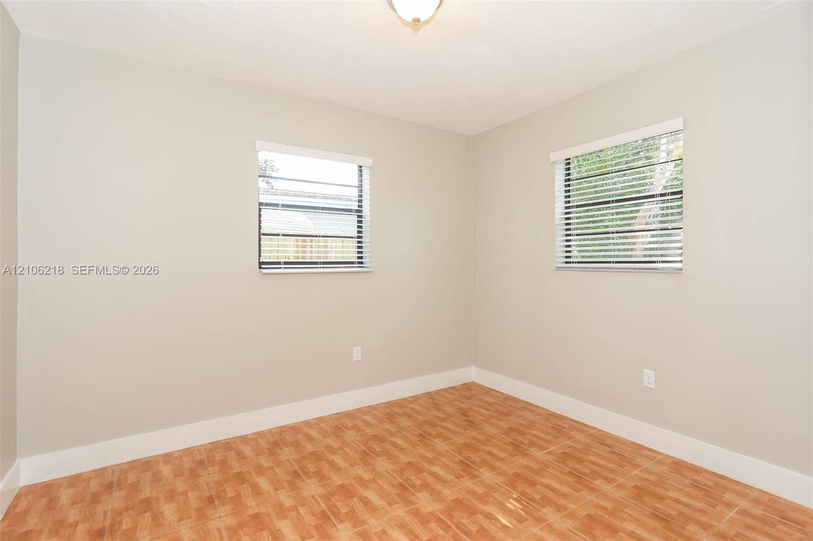 Neutral-toned interior walls, patterned tile flooring, and dual windows equipped with horizontal blinds