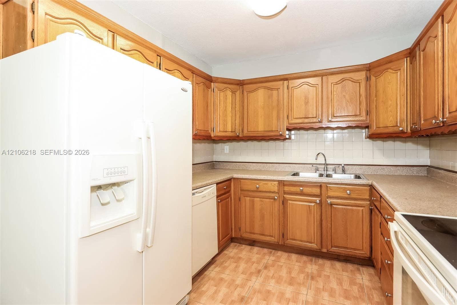 Kitchen featuring medium-tone wood cabinetry, solid-surface countertops, a double-basin stainless steel sink, and tile backsplash