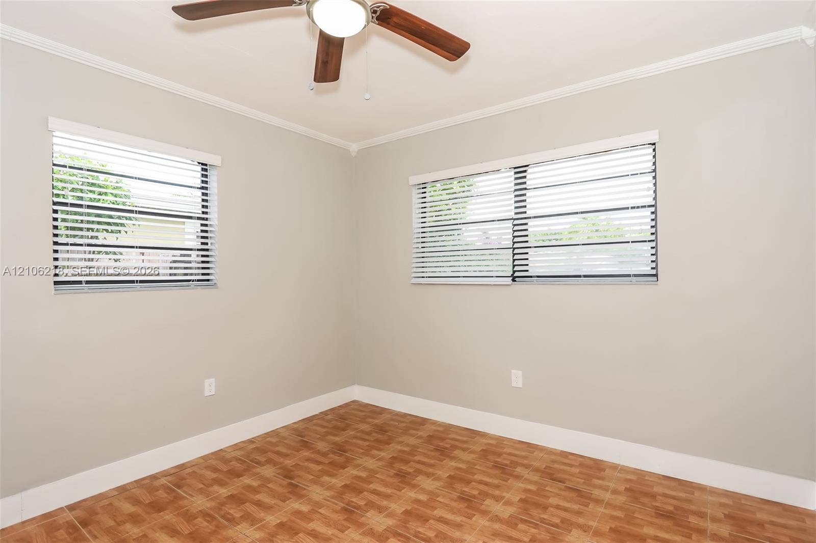 Neutral-toned walls, tile flooring with a basket-weave pattern, two windows with horizontal blinds, and a ceiling-mounted light fixture with a fan