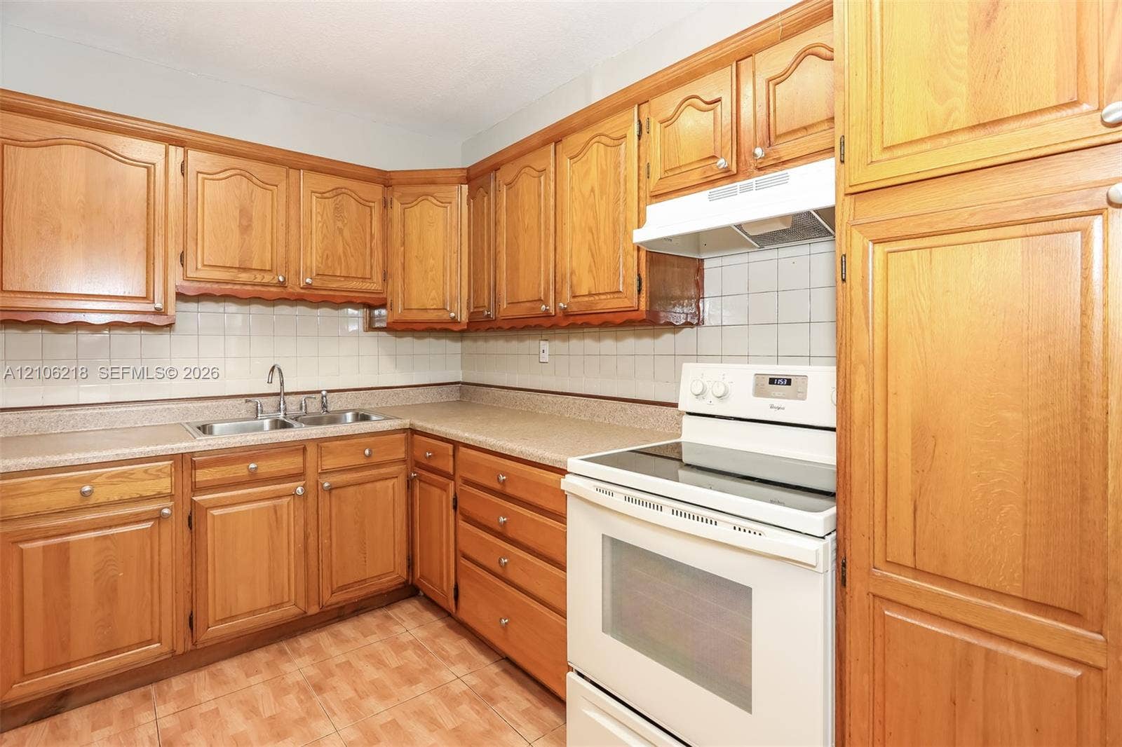 Kitchen featuring wood cabinetry, laminate countertops, a double-basin stainless steel sink, a white electric range, and tile flooring