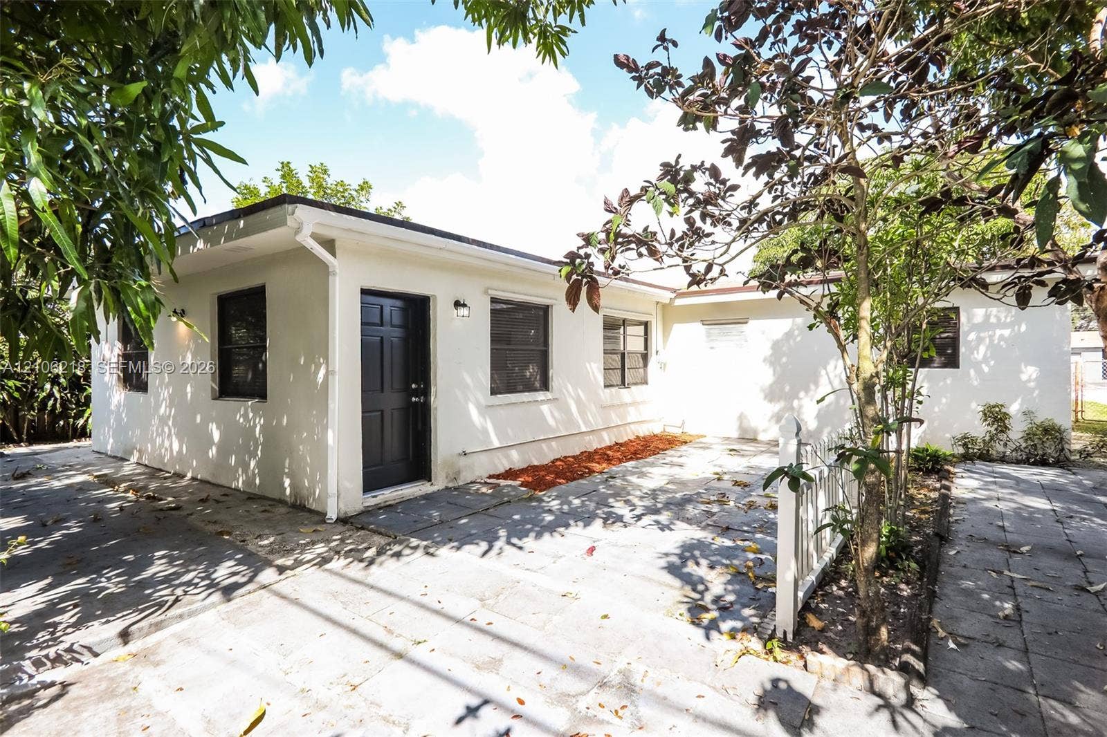 Stucco exterior featuring a paved patio, dark-toned entry door, multi-pane windows, and attached exterior lighting