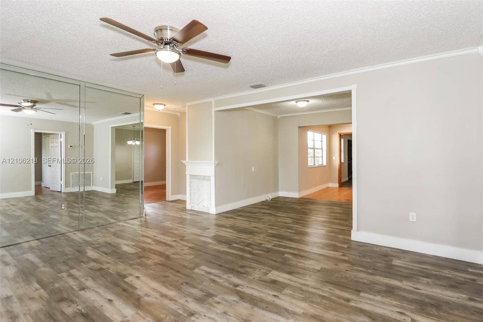 Wood-finish flooring, mirrored wall paneling, ceiling fan with integrated lighting, and fireplace with a decorative mantel