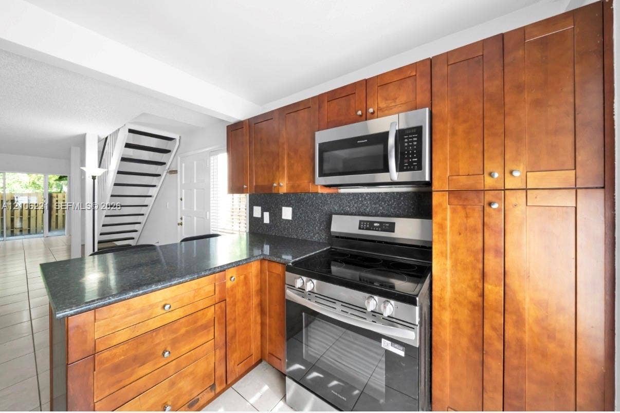 Kitchen featuring shaker-style wood cabinetry, dark stone-finish countertops, stainless steel electric range, built-in stainless steel microwave, and tile flooring