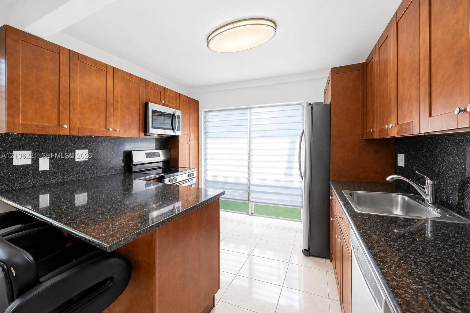 Kitchen featuring stained wood cabinetry, stone countertops, stainless steel appliances, tile flooring, and sliding glass doors