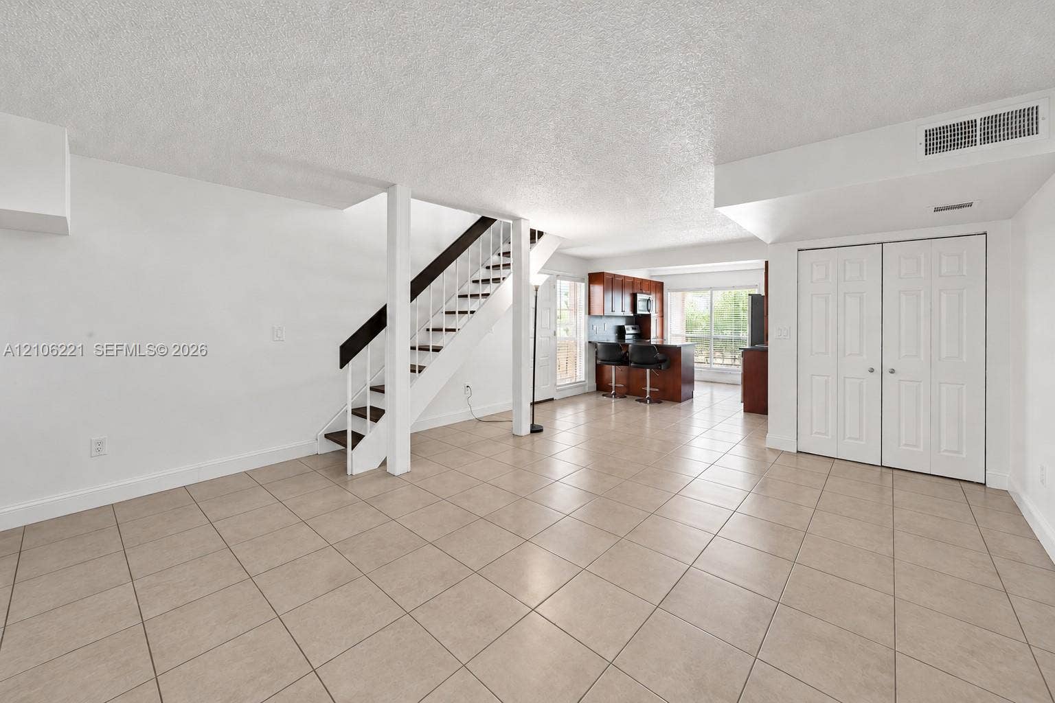 Open-concept interior featuring large-format ceramic tile flooring, a central staircase with wood treads and white risers, and dual-panel closet doors