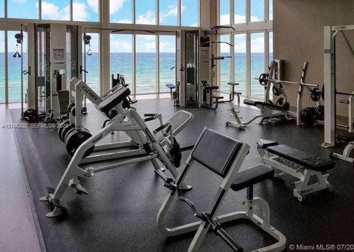 Fitness center featuring floor-to-ceiling windows, ocean horizon exposure, and resilient rubberized flooring