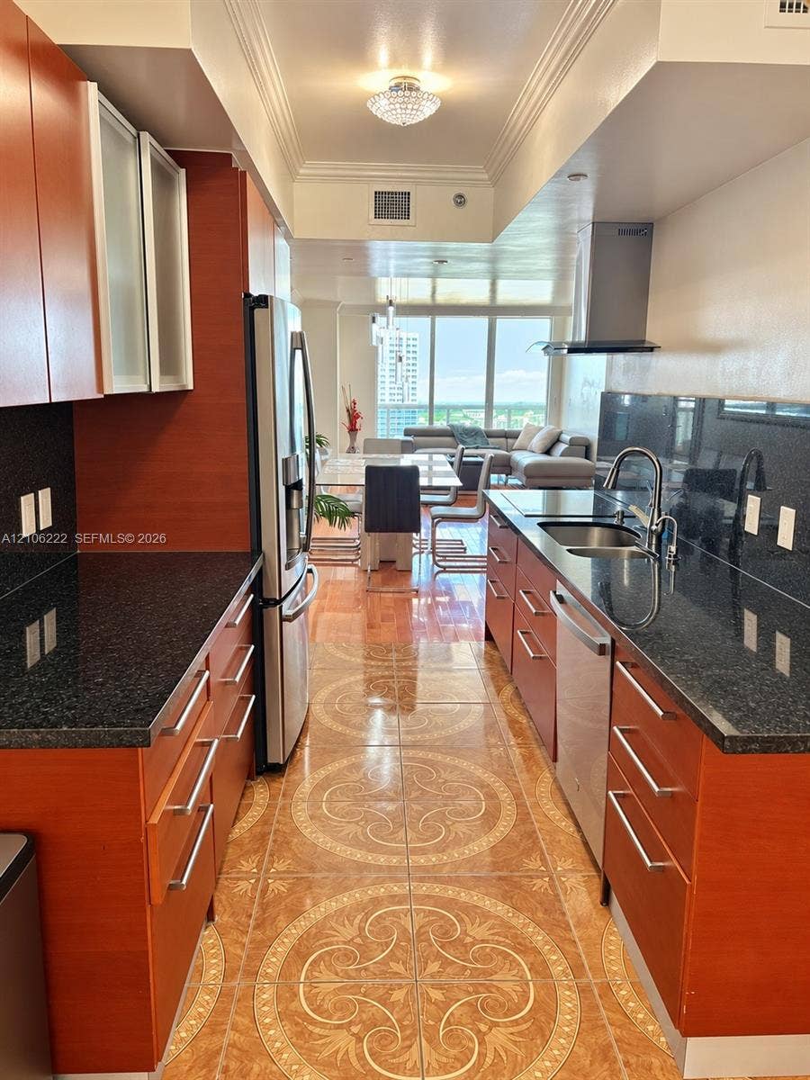 Kitchen featuring rich wood-finish cabinetry, dark stone countertops, patterned ceramic tile flooring, stainless steel appliances, and a modern stainless steel range hood