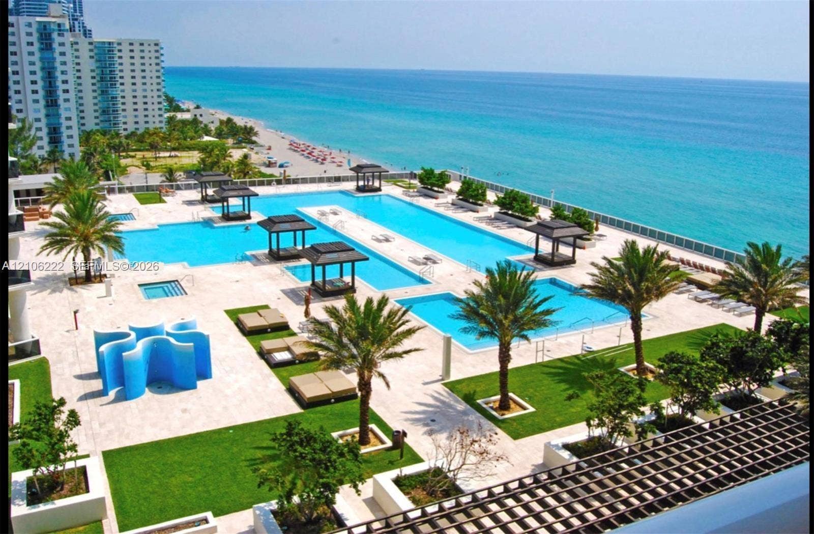 Extensive pool deck featuring multiple swimming pools, stone-paved terrace, built-in shaded cabanas, and manicured landscaping
