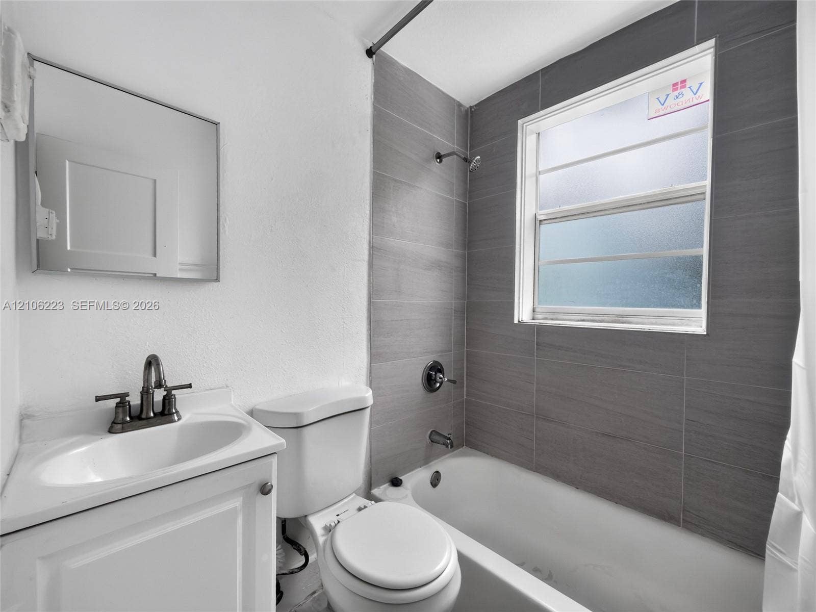 Bathroom featuring a white vanity with an integrated basin, widespread faucet, rectangular mirror, and a tub-shower combination with grey horizontal wall tile