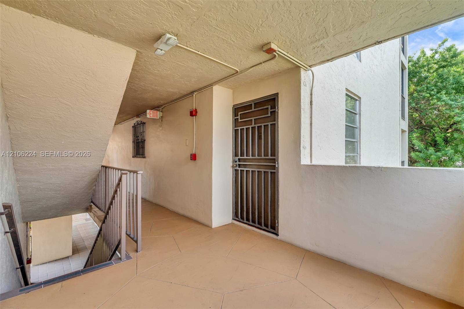 8887 Fontainebleau Boulevard, #206, Miami, Miami, FL 33172 Covered exterior walkway featuring textured stucco walls, tiled flooring, metal security door, and railing-enclosed stairwell