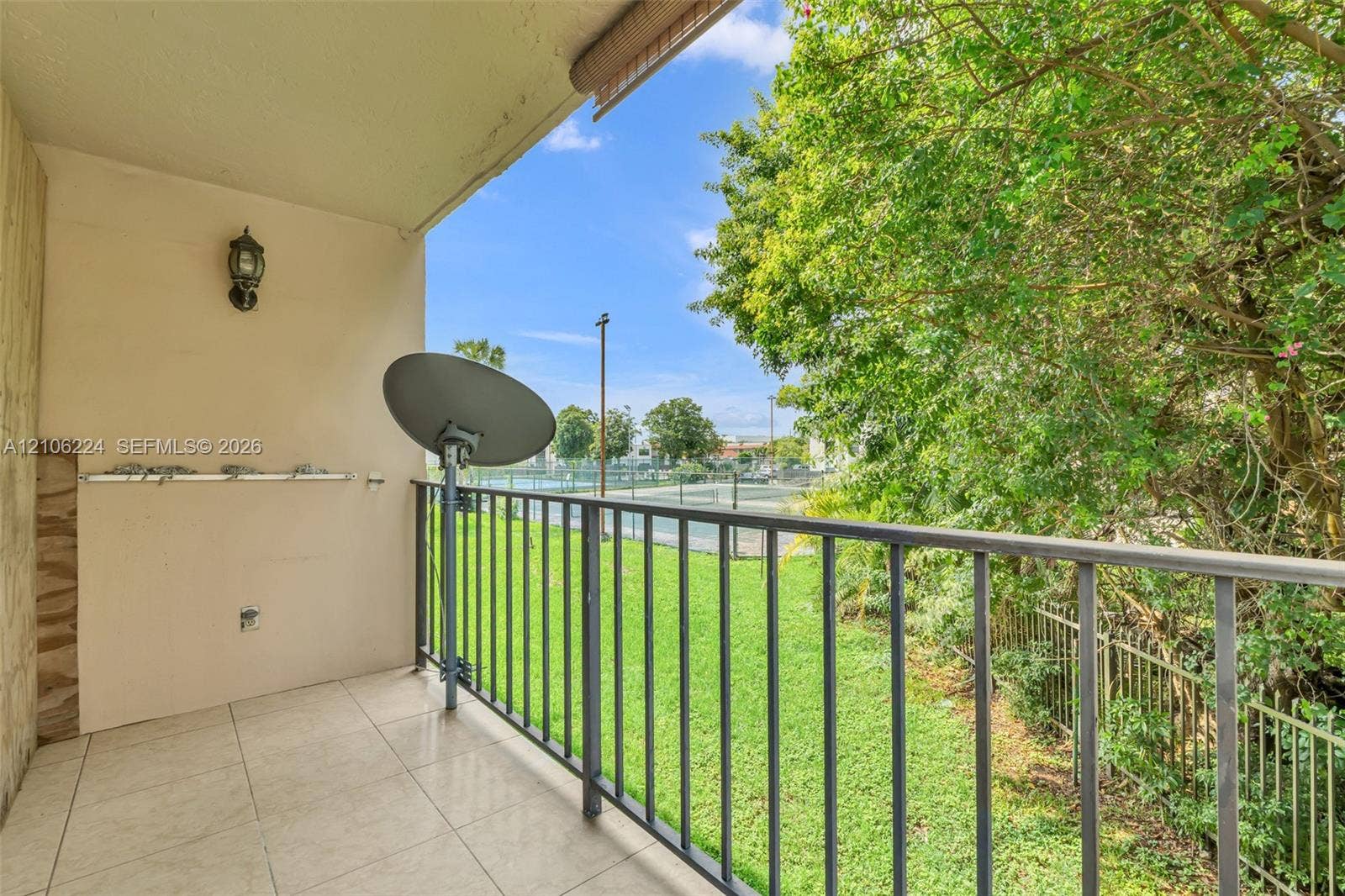 8887 Fontainebleau Boulevard, #206, Miami, Miami, FL 33172 Covered balcony featuring tile flooring, metal railing, wall-mounted exterior light fixture, and mature tree backdrop