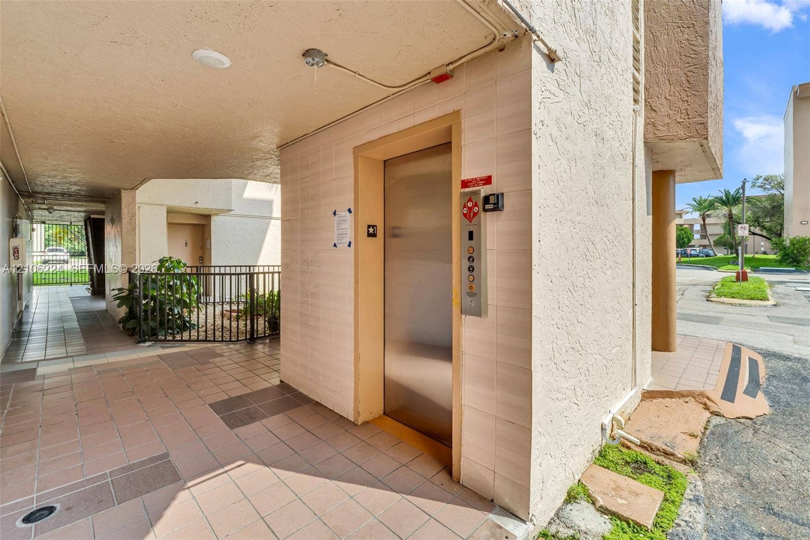 8887 Fontainebleau Boulevard, #206, Miami, Miami, FL 33172 Building exterior featuring a tiled ground-level corridor, metallic elevator doors, and a wrought iron perimeter fence