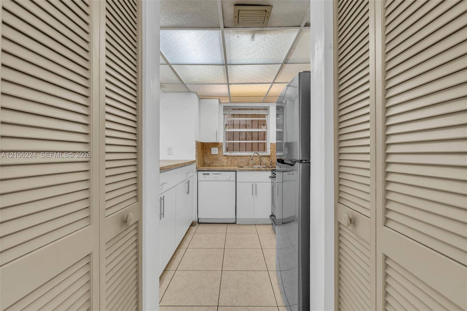 8887 Fontainebleau Boulevard, #206, Miami, Miami, FL 33172 Kitchen area featuring white cabinetry, light-toned stone-finish countertops, stainless steel appliance suite, tile flooring, and louvered closet doors