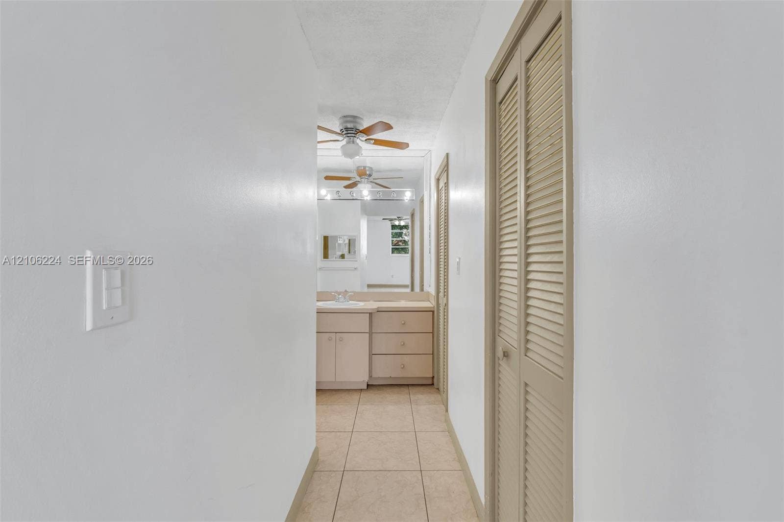8887 Fontainebleau Boulevard, #206, Miami, Miami, FL 33172 Hallway featuring tile flooring, dual louvered closet doors, and a vanity with integrated cabinetry, capped by a large wall-mounted mirror and ceiling-mounted paddle fan