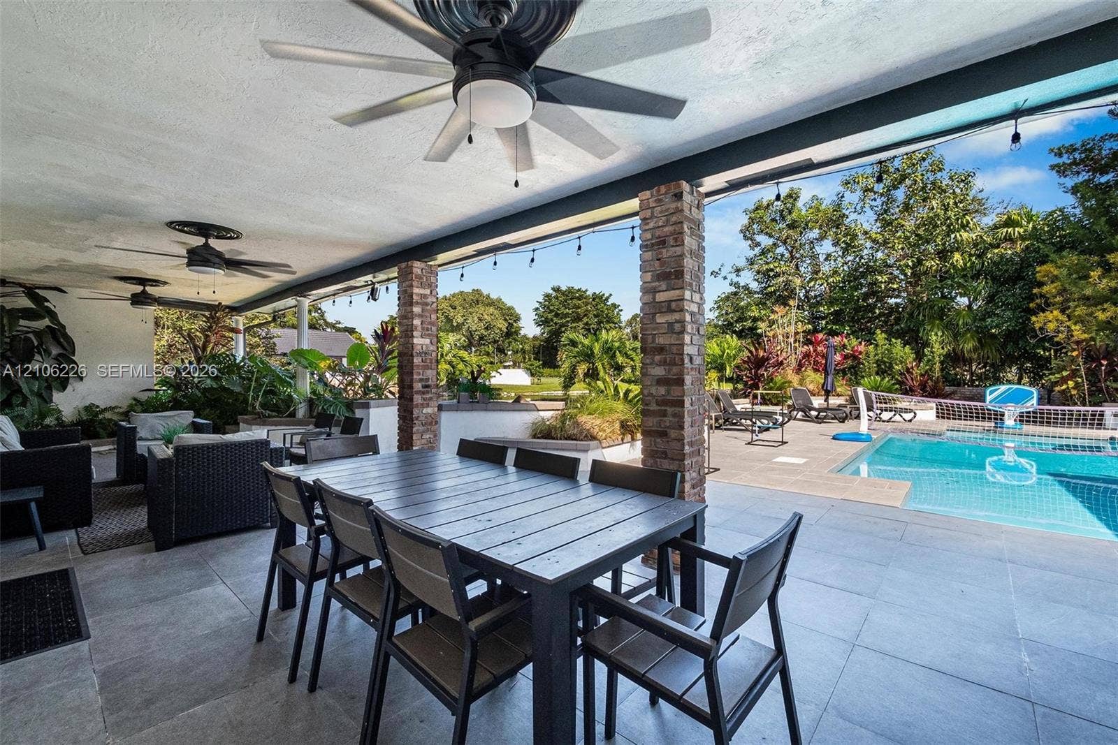 11155 SW 40th Street, Davie, FL 33328 Covered patio featuring large-format stone-style tile flooring, brick columns, and ceiling fans, opening onto a swimming pool with a stone pool deck