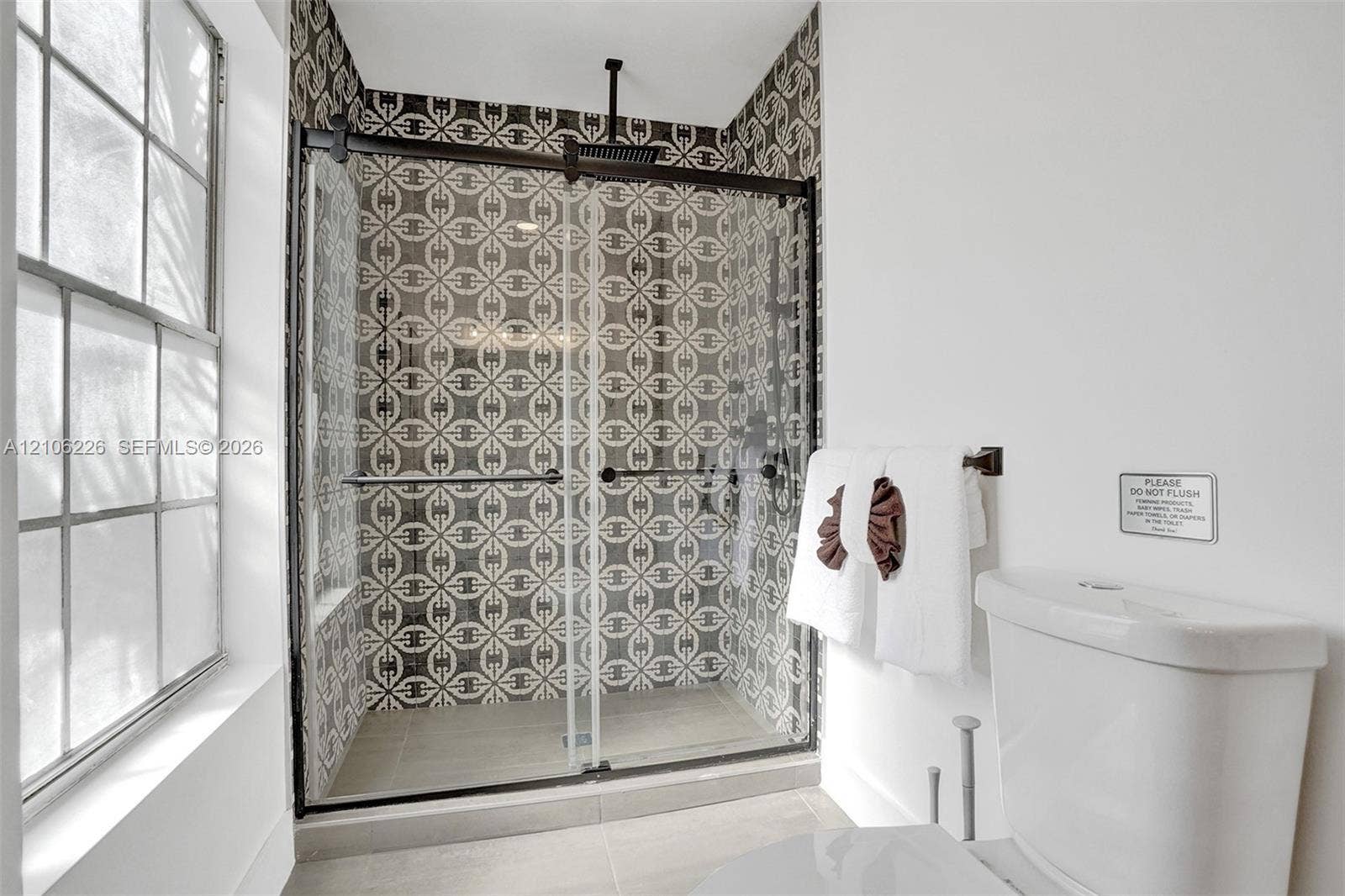 11155 SW 40th Street, Davie, FL 33328 Walk-in shower featuring patterned tile walls, sliding glass enclosure, matte black hardware, and an overhead rain showerhead