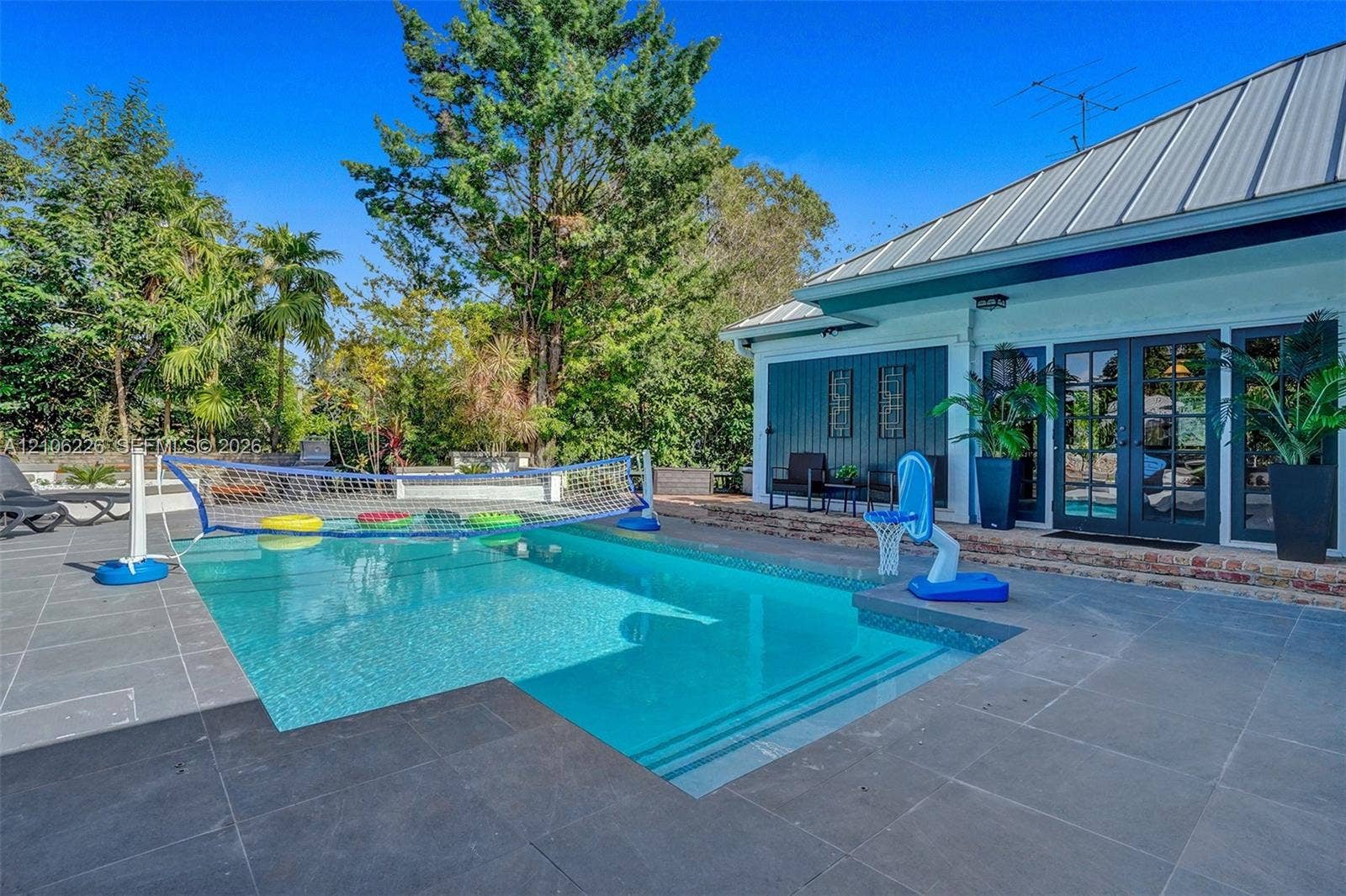 11155 SW 40th Street, Davie, FL 33328 Swimming pool with integrated steps, surrounded by large-format stone pavers, metal roofing, and dark-finished exterior siding with glass-paneled double doors