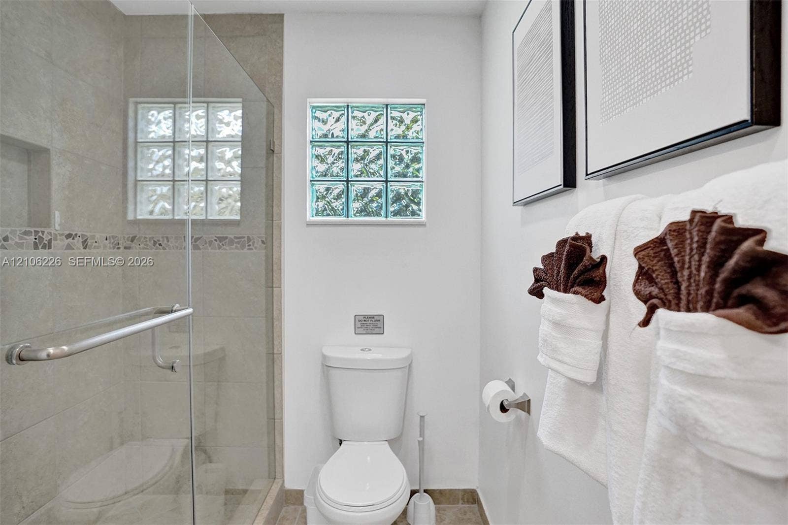 11155 SW 40th Street, Davie, FL 33328 Walk-in shower with a glass enclosure, neutral tile surround, and built-in recessed niche, complemented by glass block windows and tile flooring