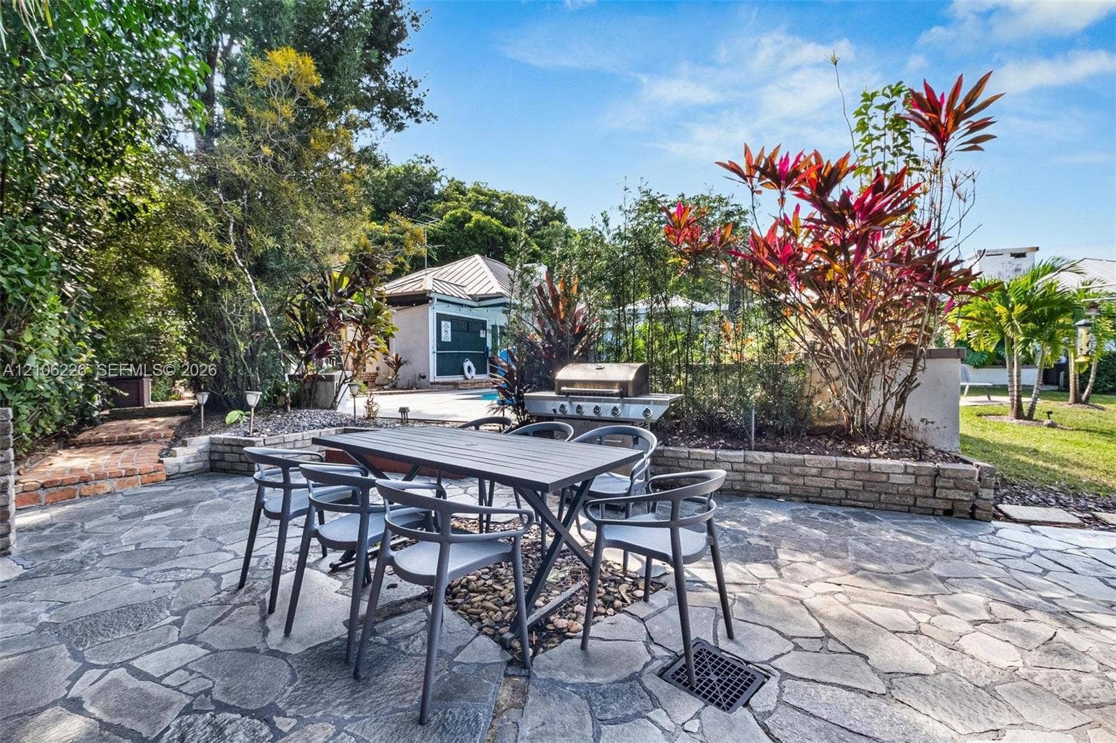 11155 SW 40th Street, Davie, FL 33328 Flagstone patio featuring a built-in outdoor grill, raised brick planter beds, and lush tropical landscaping