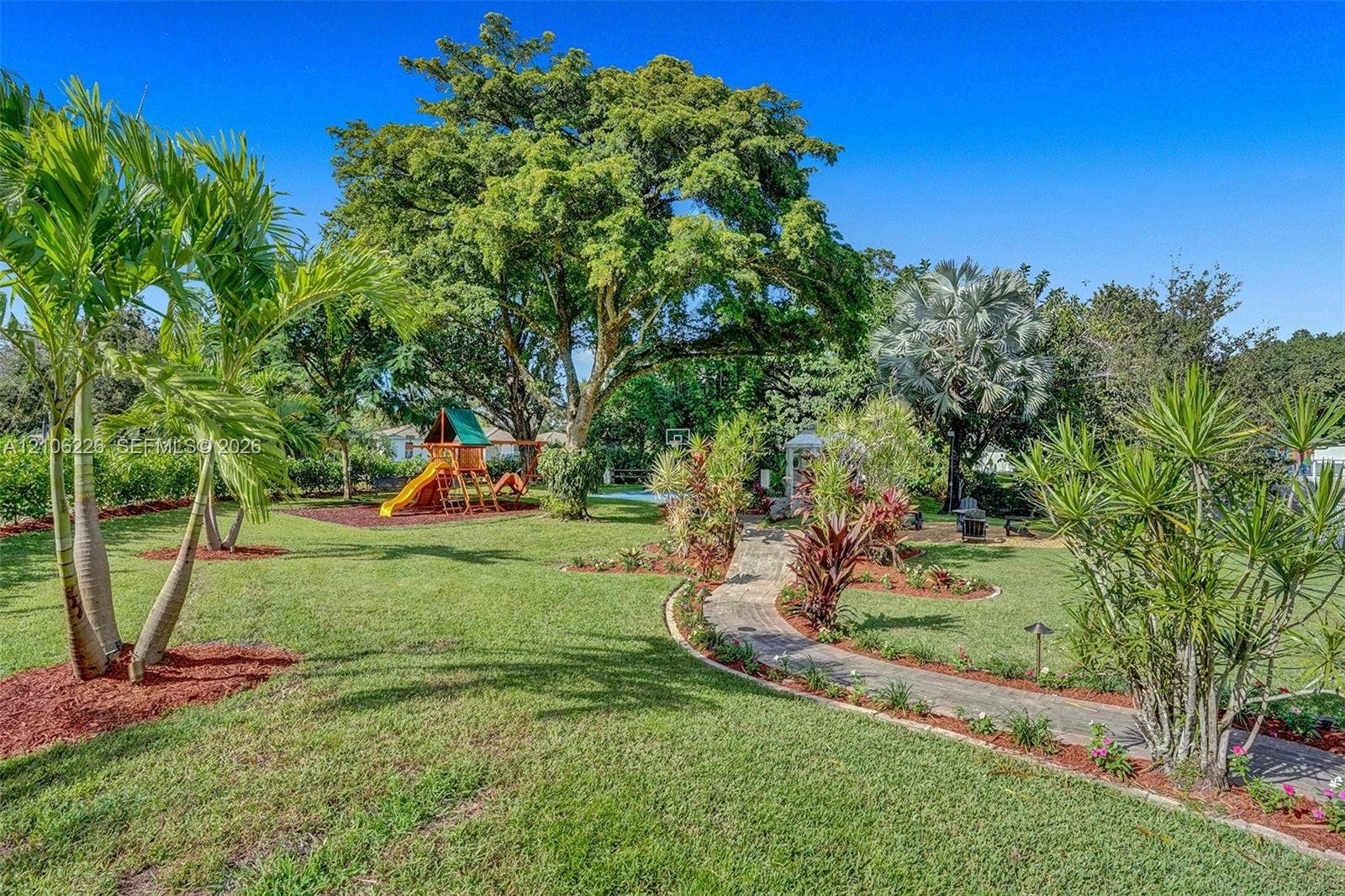 11155 SW 40th Street, Davie, FL 33328 Expansive backyard featuring mature shade trees, established tropical landscaping, a stone-paver pathway, and mulch-bedded plant borders