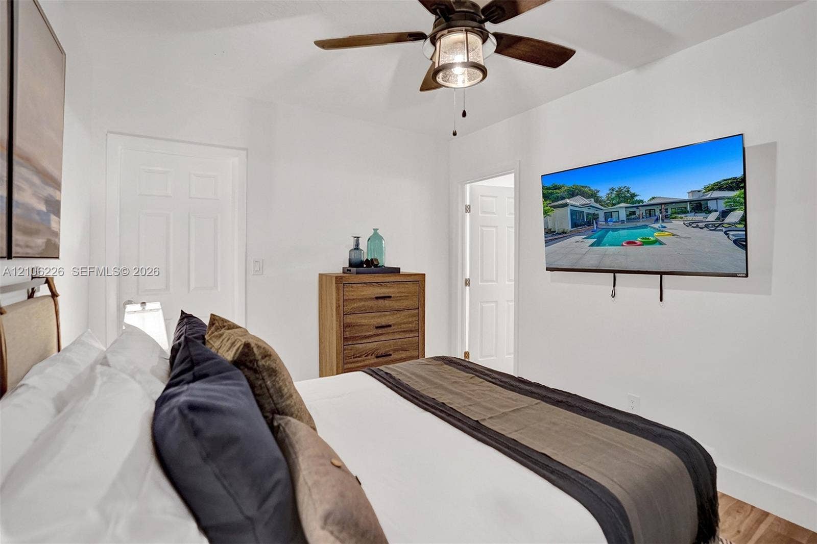 11155 SW 40th Street, Davie, FL 33328 Neutral-toned bedroom featuring wood-finish flooring, a ceiling fan with integrated lighting, and multiple paneled doors