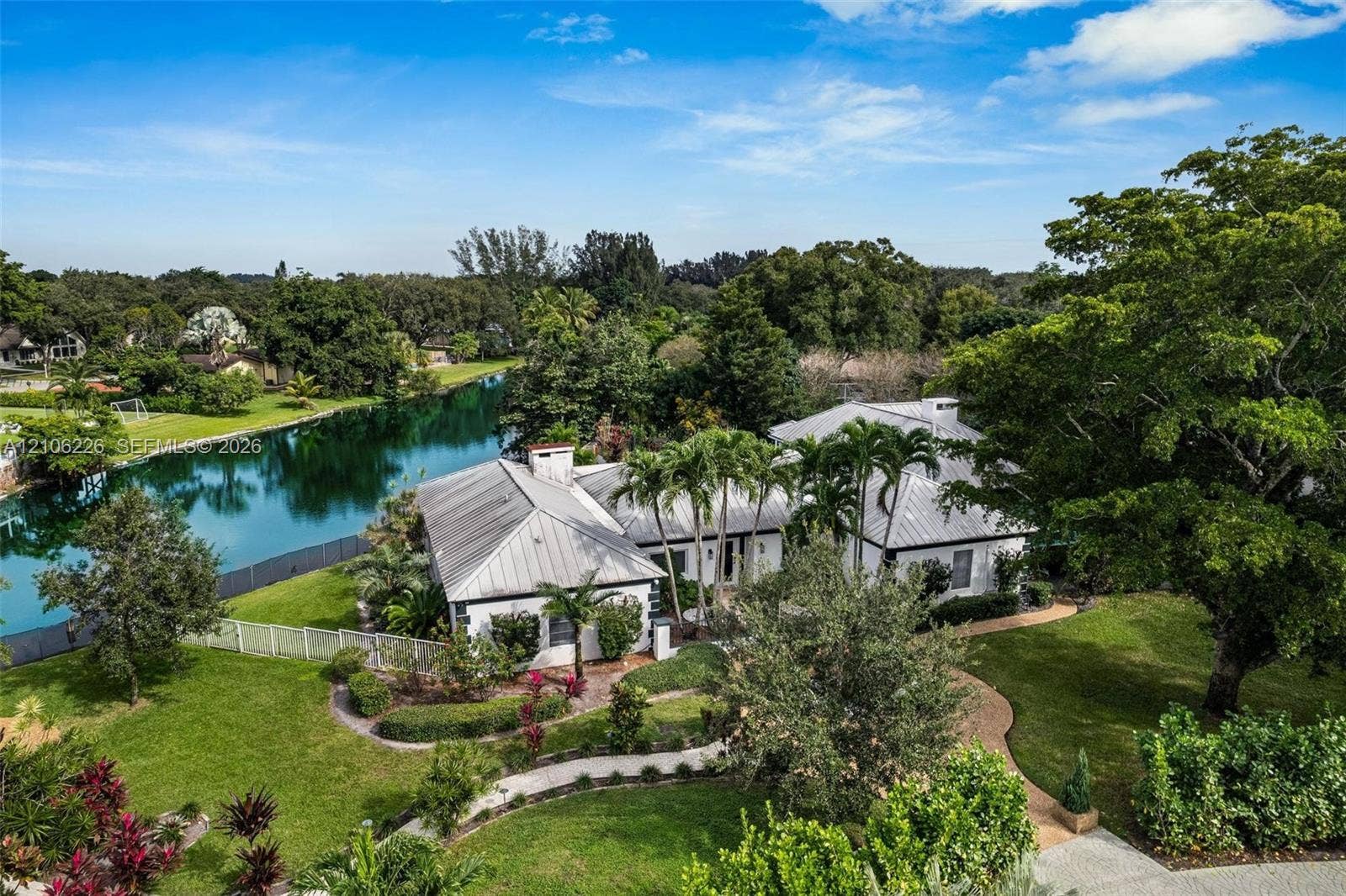 11155 SW 40th Street, Davie, FL 33328 Waterfront estate featuring a metal roof, landscaped grounds, a paved walkway, and mature trees