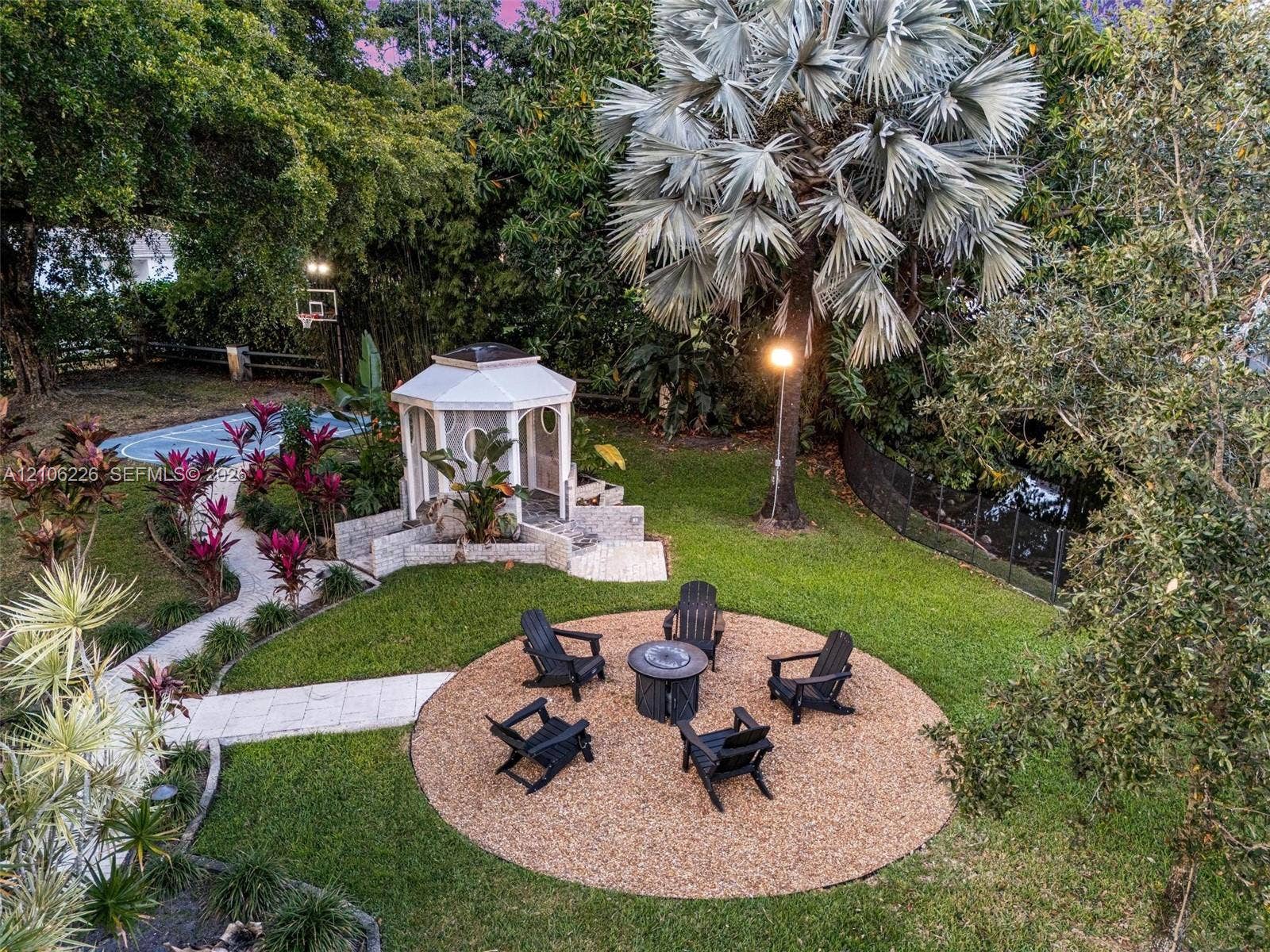 11155 SW 40th Street, Davie, FL 33328 Landscaped grounds featuring a stone-paved pathway, a detached hexagonal gazebo with stone terracing, a circular pea-gravel patio, and a dedicated athletic court
