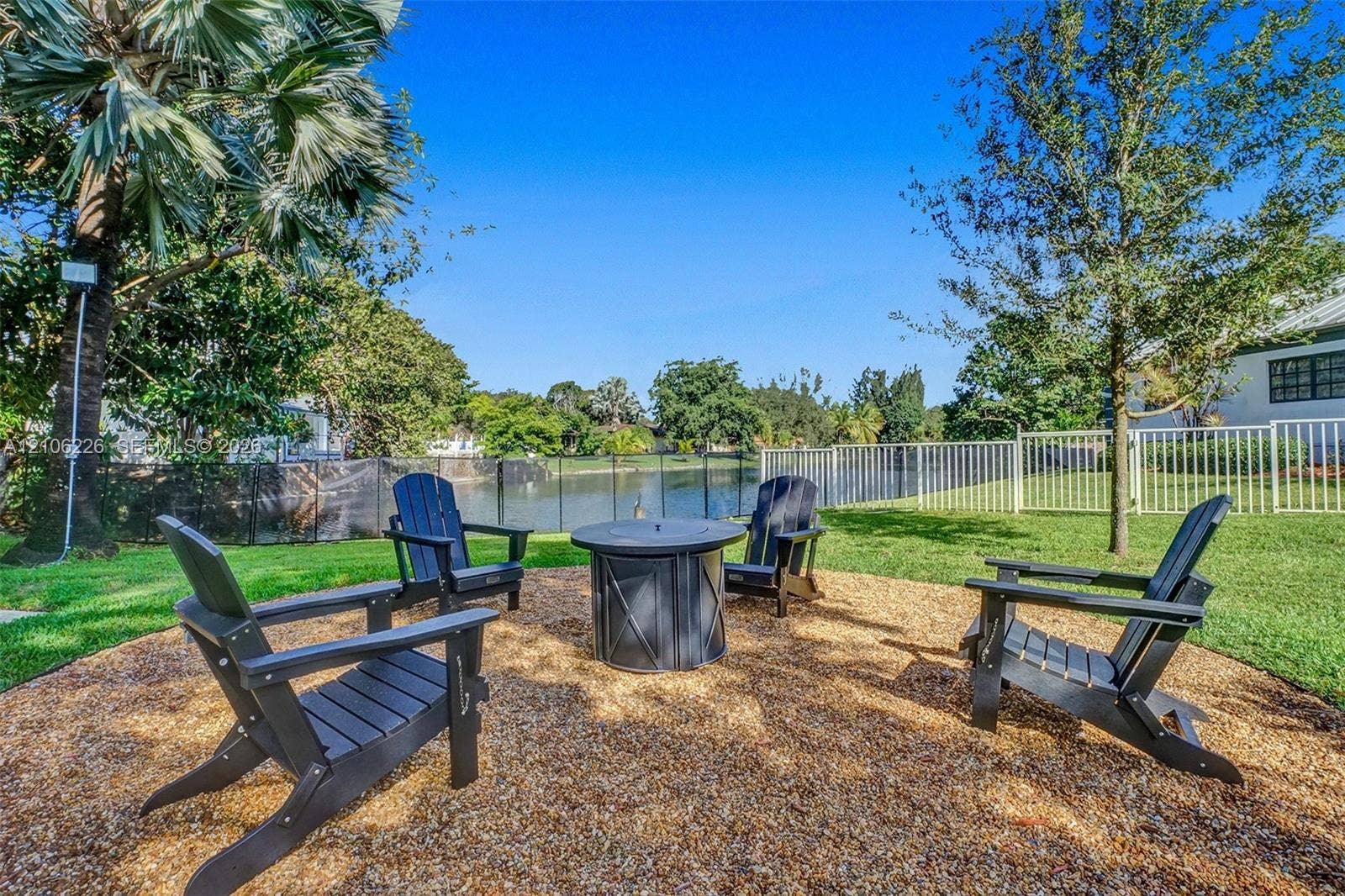 11155 SW 40th Street, Davie, FL 33328 Backyard area featuring a circular wood-mulched patio, a built-in metal fire pit, and a black mesh perimeter fence overlooking a water feature