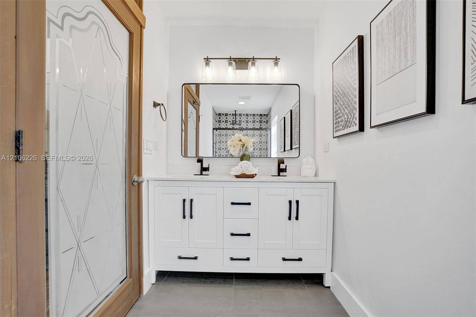 11155 SW 40th Street, Davie, FL 33328 Double vanity featuring white cabinetry, black hardware, a rectangular framed mirror, three-light glass fixture, and dual faucets