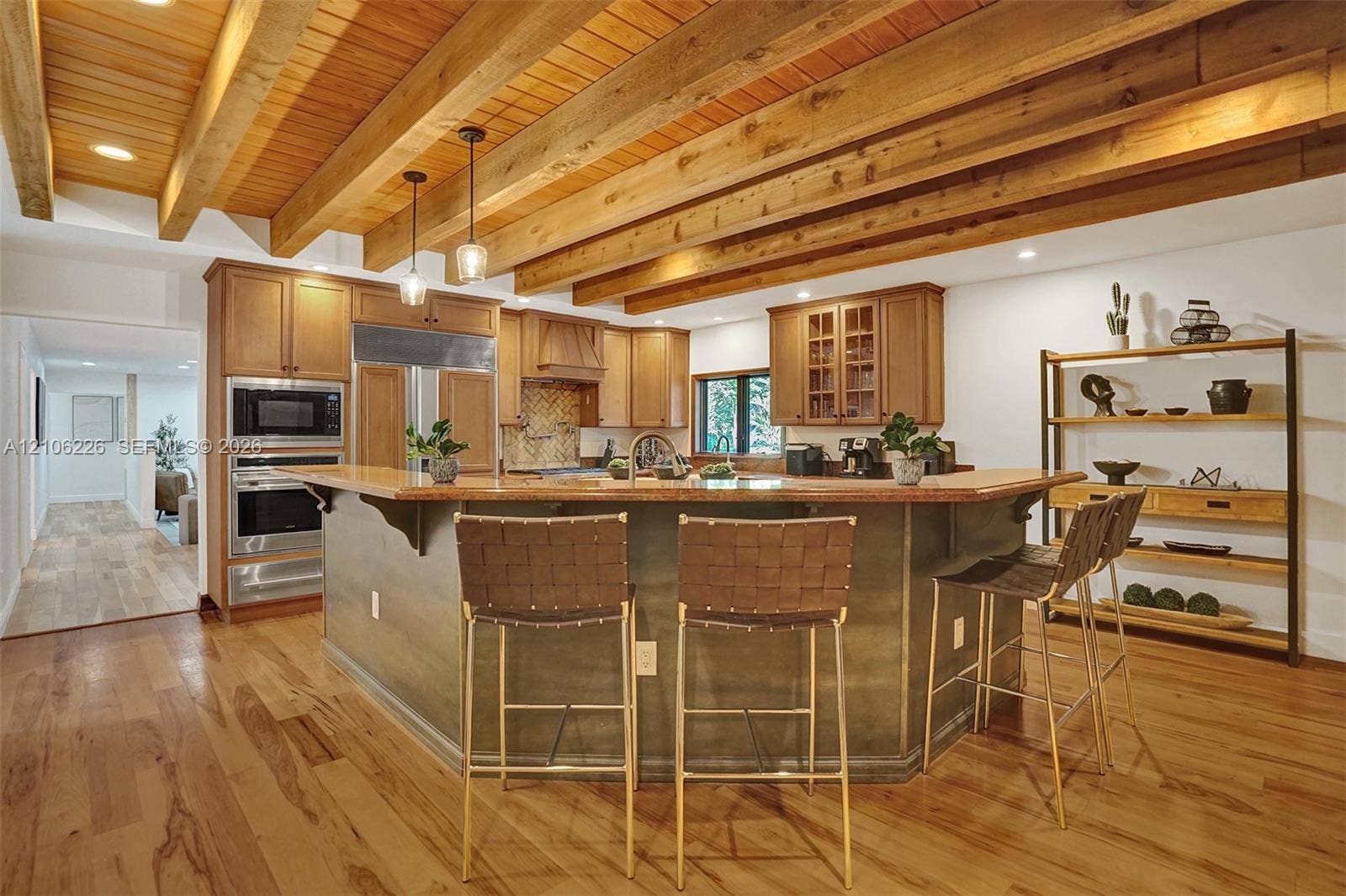 11155 SW 40th Street, Davie, FL 33328 Kitchen featuring exposed natural wood ceiling beams, wood-finish flooring, wood cabinetry, stainless steel built-in appliances, and a center island with countertop seating