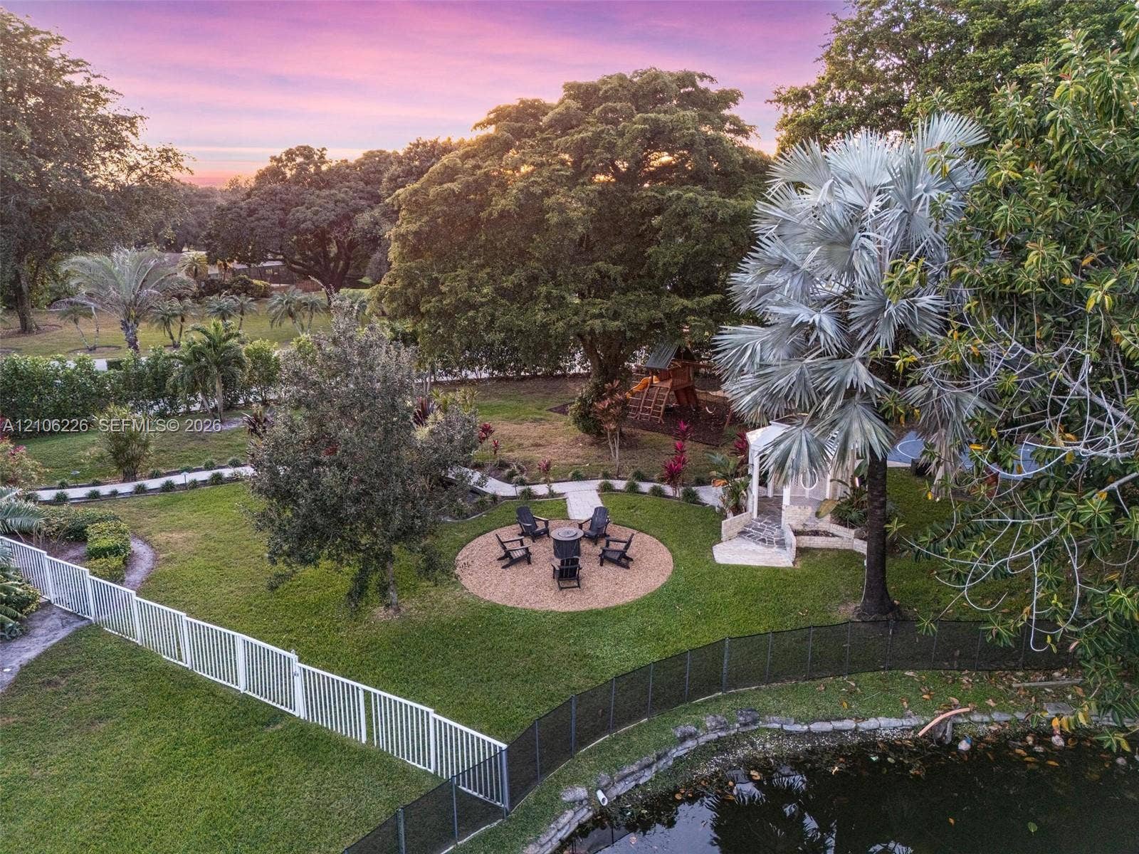 11155 SW 40th Street, Davie, FL 33328 Expansive grounds featuring a circular gravel patio, mature trees, landscaped greenery, and a private pond with stone edging