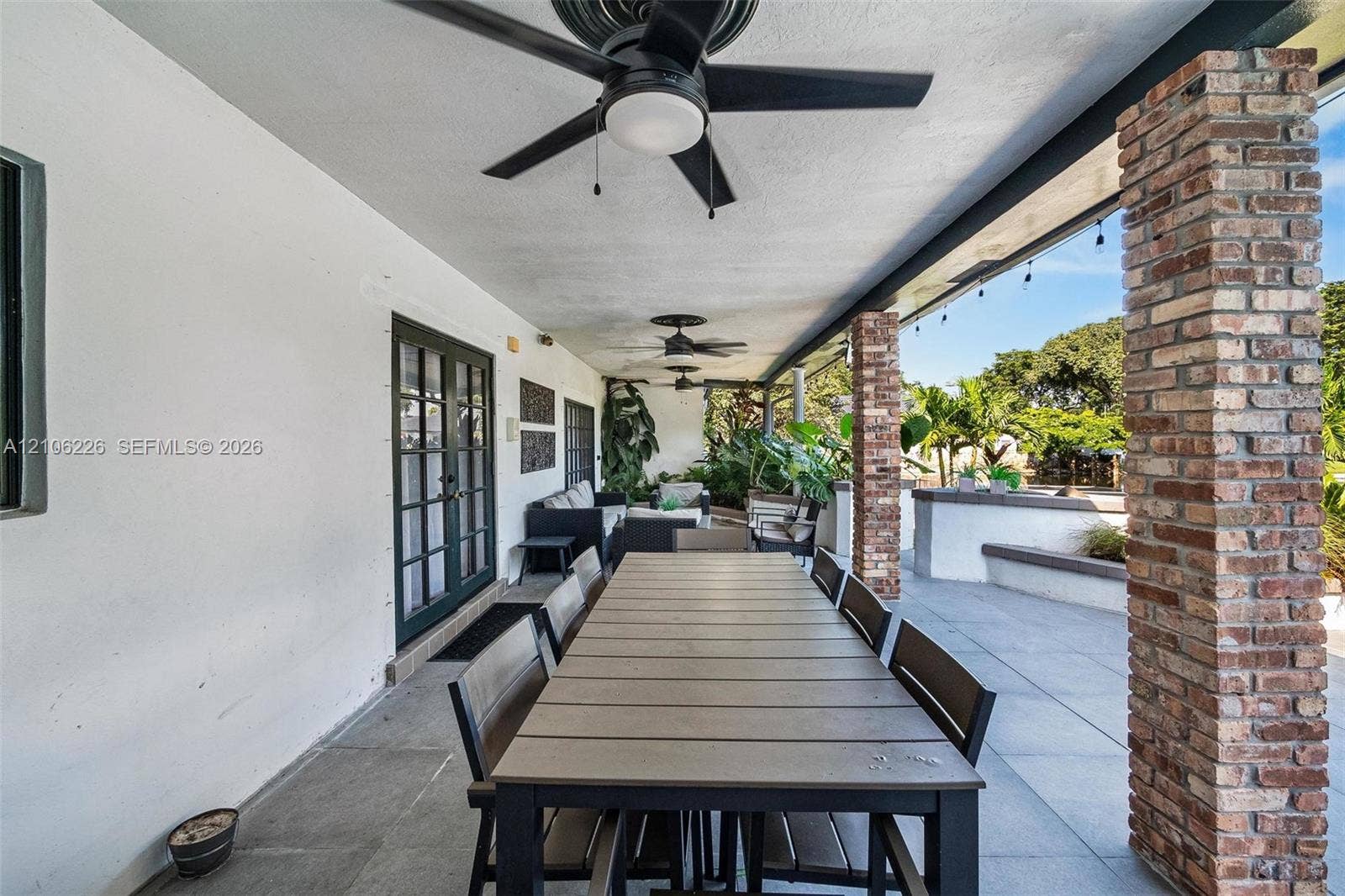 11155 SW 40th Street, Davie, FL 33328 Covered patio featuring large-format stone flooring, exposed brick structural pillars, dual ceiling fans, and integrated string lighting